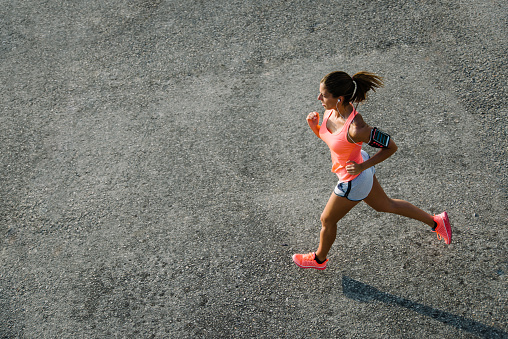 Top view of sporty young fit woman running on urban asphalt. Female athlete training outside in summer.