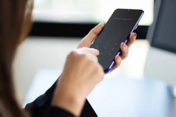 Photo of Woman holding a mobile phone using her finger to press the unlock code.