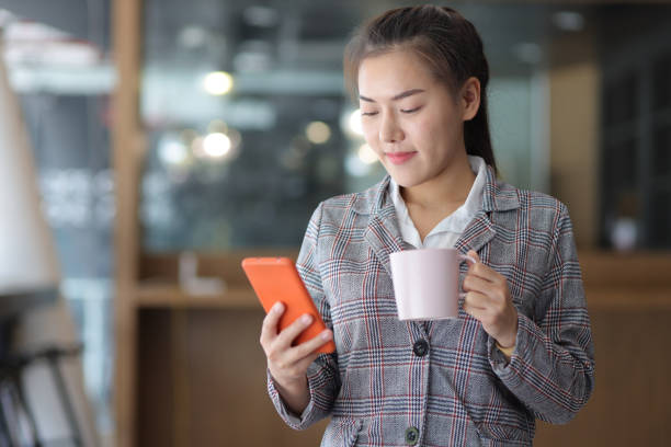 istock Asian businesswoman using mobile phone to read and text while drinking coffee. 1404688213