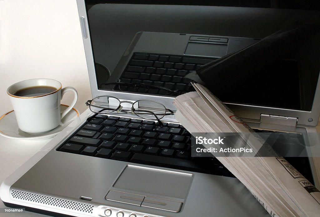 Technology and Old-Fashioned Job Searching A cup of coffee or tea next to a laptop, with eyeglasses and a rolled up newspaper on top of it. Porcelain Stock Photo