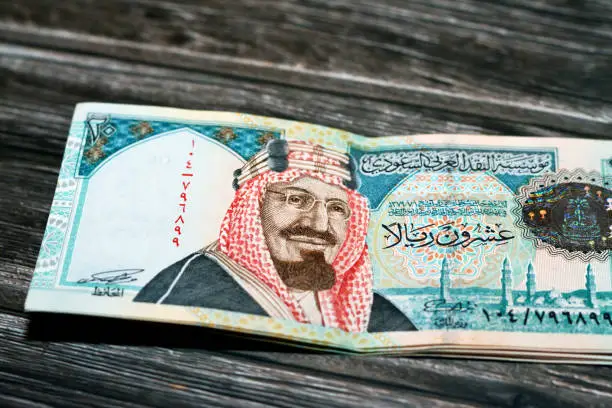 Stack of Saudi Arabia 20 SAR twenty Saudi riyals cash money banknote with the photo of king AbdulAziz Al Saud and Quba mosque in Madinah isolated on a wooden background, selective focus
