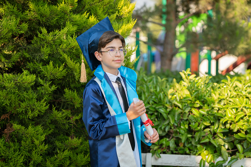 Teenage boy wearing cap and gown holding diploma in schoolyard