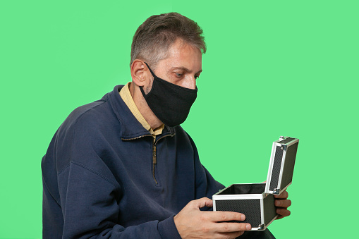 Secret mission. A man in a black protective mask opens a case isolated on green chroma key background