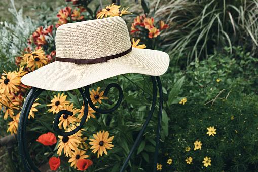Women's summer hat on a green chair in a garden with flowers, nature and slow life concept