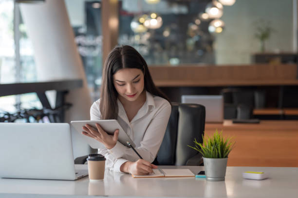 istock Young Asian businesswoman taking notes using a tablet at the modern office. 1404709988