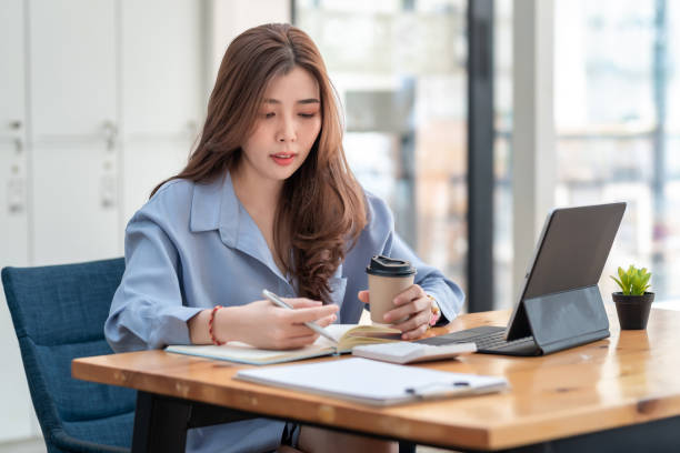 istock Asian businesswoman holding coffee working at the office using a tablet. 1404710041