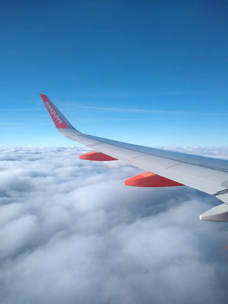 In flight - Wing of Easyjet commercial airliner viewed in blue sky above cloud canopy