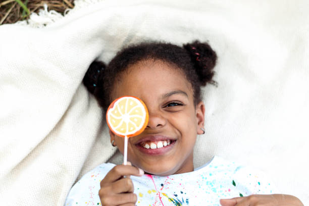 Happy African-American girl with a lollipop in her hands is lying on a blanket at a picnic in the park,top view.Summer concept,diverse people