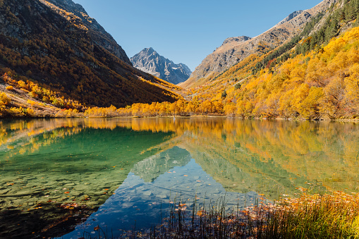 Lake with transparent water and colorful autumnal trees. Mountains and lake