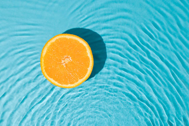 istock Minimal summer flat lay with half fresh oranges in fresh sunny water. Creative organic fruit background. 1404719517