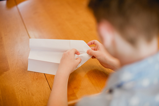 A teenage boy making a paper airplane. Shot indoors with all natural light.