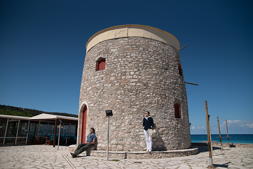 Friends on Vacation Enjoying Seaside Sun and Air at a Beautiful Stone Windmill of Lefkada Island in Greece
