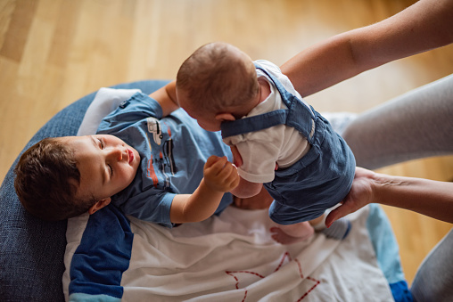 Boy holding hands of his newborn baby brother while lying at home