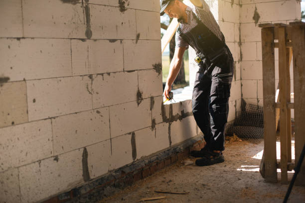 istock Construction worker at construction site measures the length of window opening and brick wall with tape measure. Cottage are made of porous concrete blocks, work clothes - jumpsuit and baseball cap 1404728663