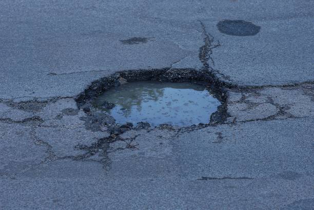 istock one pit pothole with dirty water on the gray asphalt road 1404731007