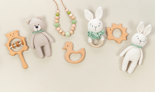 Baby toys background. Knitted bunny, handmade teddy bear and wooden teethers for banner on a pastel beige banner. Wooden rattles and toys for a cute baby banner with copy space.