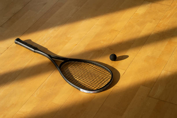 raqueta de squash negro y pelota con iluminación natural en cancha gris. póster horizontal de temas deportivos, tarjetas de felicitación, encabezados, sitio web y aplicación - squash racketball sport exercising fotografías e imágenes de stock