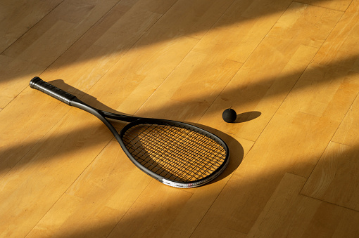 Black squash racket and ball with natural lighting on grey court. Horizontal sport theme poster, greeting cards, headers, website and app