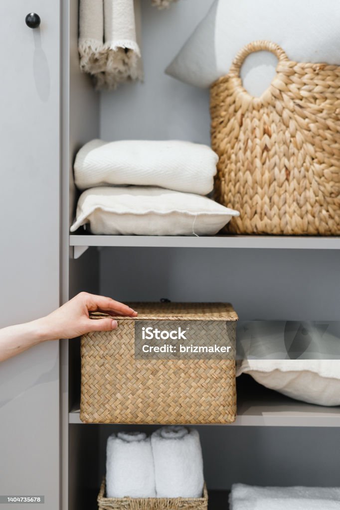 Housewife puts wicker box with clothes on wardrobe shelf Cropped view of neat housewife puts wicker box with clothes on wardrobe shelf, during general cleaning by modern storage system. Concept of comfortable organization of space in apartment Organization Stock Photo