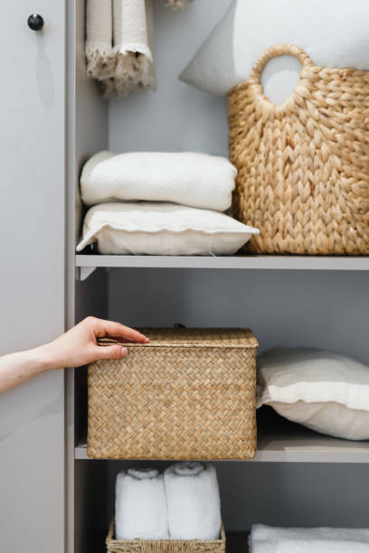 Housewife puts wicker box with clothes on wardrobe shelf Cropped view of neat housewife puts wicker box with clothes on wardrobe shelf, during general cleaning by modern storage system. Concept of comfortable organization of space in apartment tidy stock pictures, royalty-free photos & images