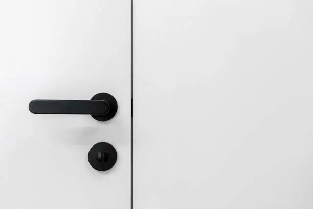 Element of interior design. Close up view of black handle with lock on entrance door in living room or bedroom. Selective focus on latch and doorknob in apartment, close to white copy space wall