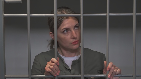 Brooding, sad woman in prison cell. Restriction of freedom.