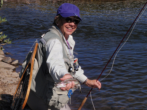 A happy senior woman fly-fisher showing off her catch.