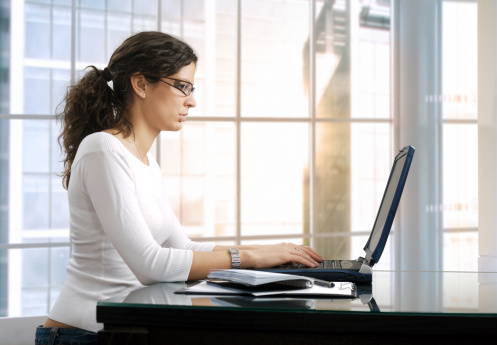 Young female office worker sits in front of her computer screen. Daylight, indoor, office. White cloth.