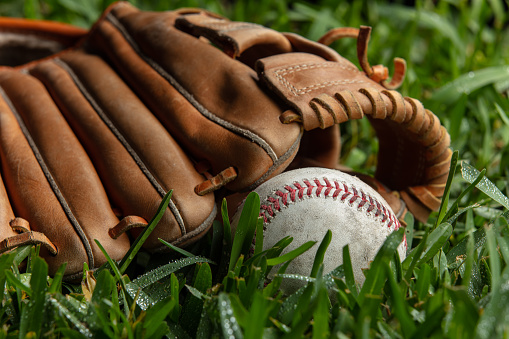 Studio shot of an old baseball resting near a catcher's mitt on grass.