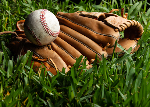 Studio shot of an old baseball resting on top of a catcher's mitt on grass.