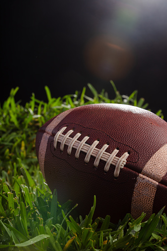 Studio shot of an old football resting on grass with black background.