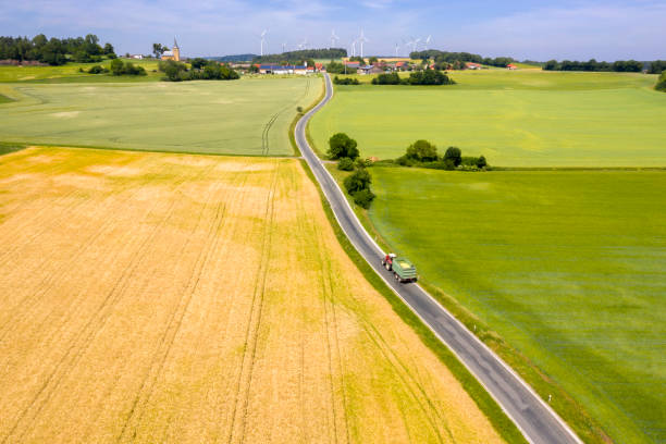 Tractor Driving on Coutry Road in Idyllic Spring Landscape, Aerial View Aerial view of a patchwork landscape with fields in spring, tractor driving on the coutry road. patchwork landscape stock pictures, royalty-free photos & images