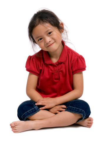 A young girl sits cross legged on the floor. 