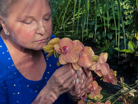 Caucasian woman is in her tranquil garden smelling orchids that she has grown.