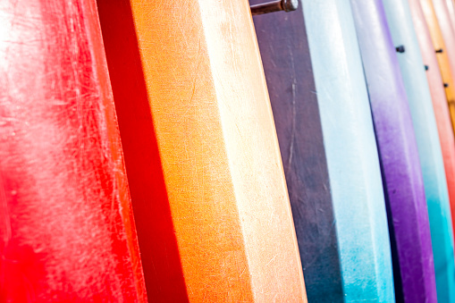 Row of many vibrant multicolor colorful red blue purple yellow kayak surfing boards surfboards boats in rental shop store in Florida abstract closeup pattern view by beach