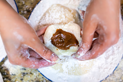 Flat top view of hands shaping cooking making mochi sticky daifuku Japanese rice cake with chocolate filling and starch flour as traditional dessert