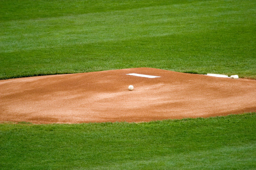A baseball resting on the pitchers mound before a game.