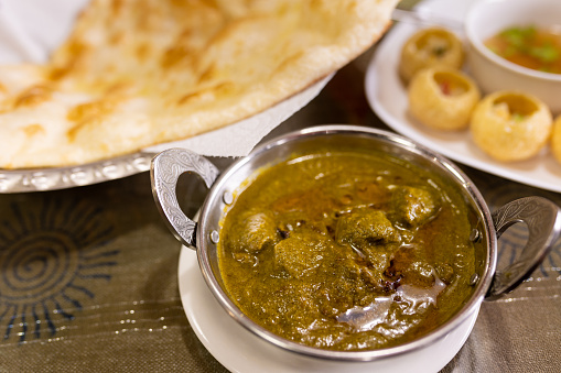 A close up of a bowl of Indian style mutton curry with Naan bread at a restaurant.
