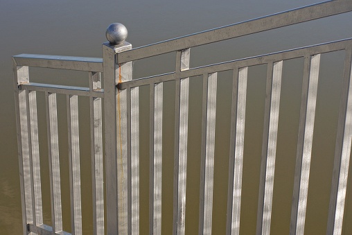 part of gray metal handrails made of iron bars over the water of the lake on the street