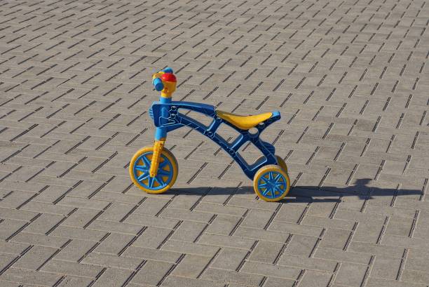 one small plastic tricycle stands on a gray sidewalk in the street
