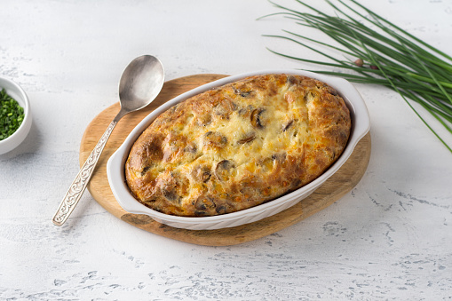 Casserole or clafoutis with mushrooms and cheese in a white ceramic baking dish sprinkled with green onions on a light background. Delicious homemade food