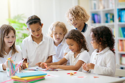 Kids go back to school. Interracial group of children of mixed age in classroom. Students learn to read and write. Preschooler or kindergarten kid with teacher. Child learning letters with flash cards