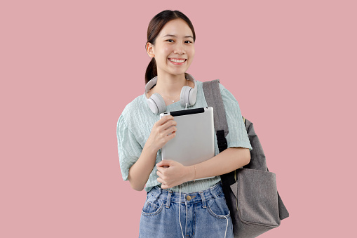 Happy Young Asian student girl holding tablet computer over isolated pink background.