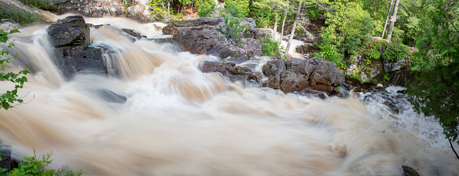The blurred water of Duchesnay Falls flows down a river through a forest in North Bay, Ontario during sunset.
