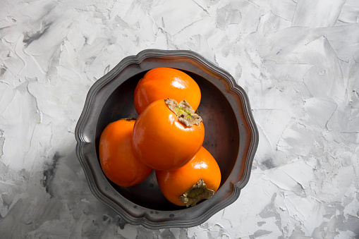 still life with persimmon on a gray cement background in a pewter dish, colorful flatley, healthy food,. High quality photo