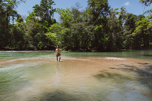 Caucasian man walking in a river in the middle of Mexican jungle on a hut sunny summer day.