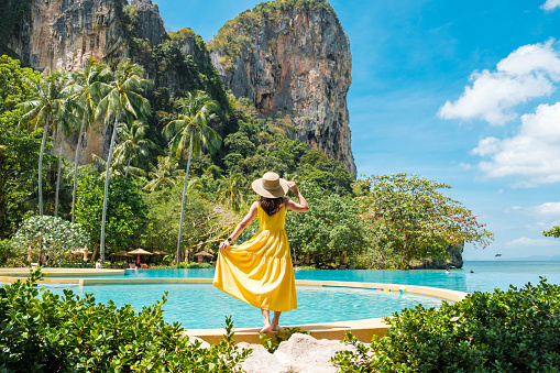 Tourist resort in the summer with woman walking next to swimming pool. 3D generated image. Generic location and architecture.