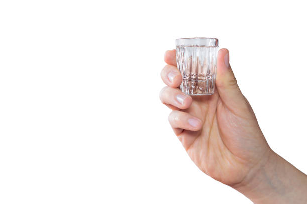 a white hand holding a shot of alcohol on a white background - shot glass glass alcohol color image imagens e fotografias de stock