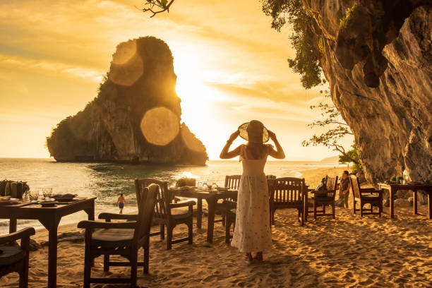 mujer turista con vestido blanco cena en la cueva del restaurante en la playa de phra nang al atardecer, railay, krabi, tailandia. vacaciones, viajes, verano, wanderlust y concepto de vacaciones - hotel restaurant women luxury fotografías e imágenes de stock