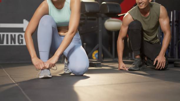 close up. active athletic asian woman in sportswear prepare to exercise tie shoelaces and warm up for body weight training or cardio in sport fitness gym. concept of healthy, lifestyle, workout, sport. - checking the time imagens e fotografias de stock